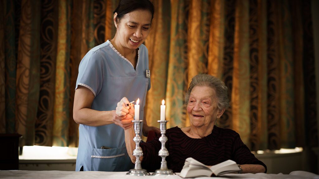 Jewish Care resident lighting candles with Jewish Care staff.
